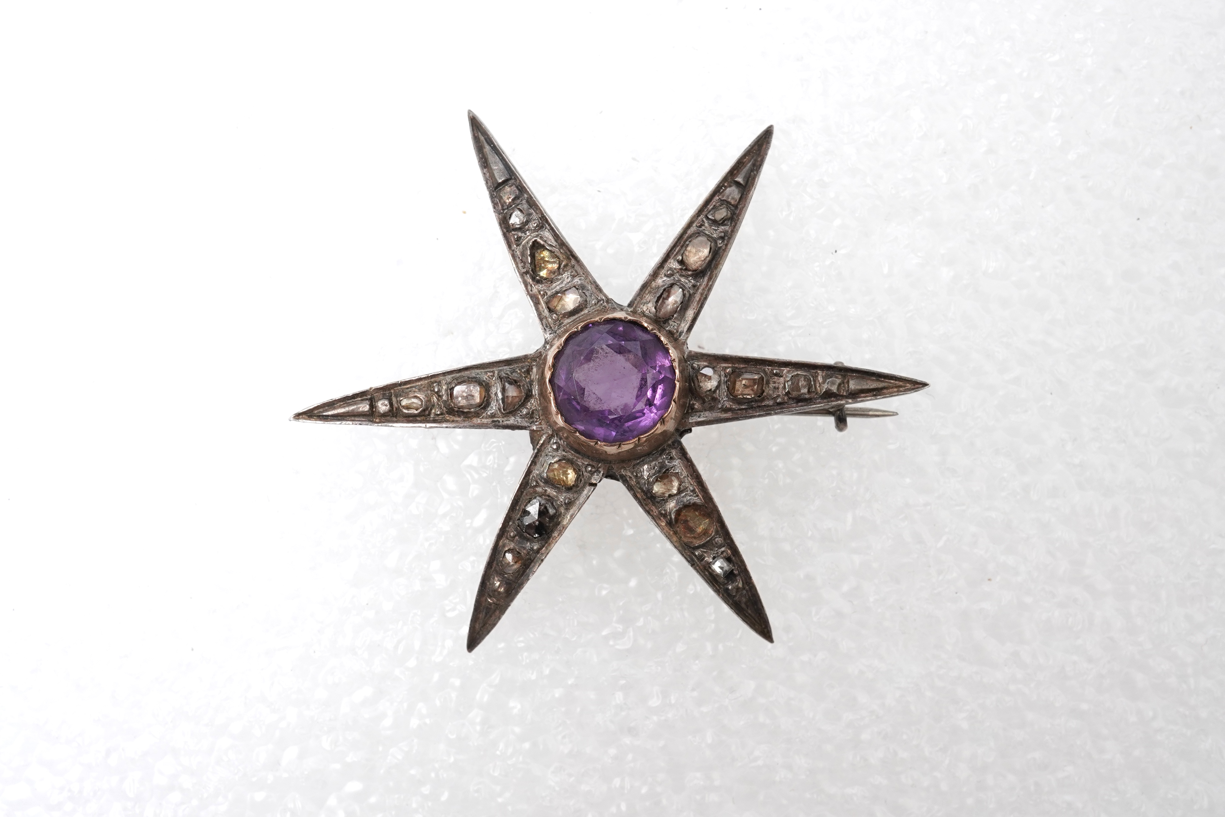 An amethyst and diamond brooch, designed as a star, set with a circular-cut amethyst and rose-cut diamonds, mounted in silver and gold, length 5.7cm, two diamonds deficient